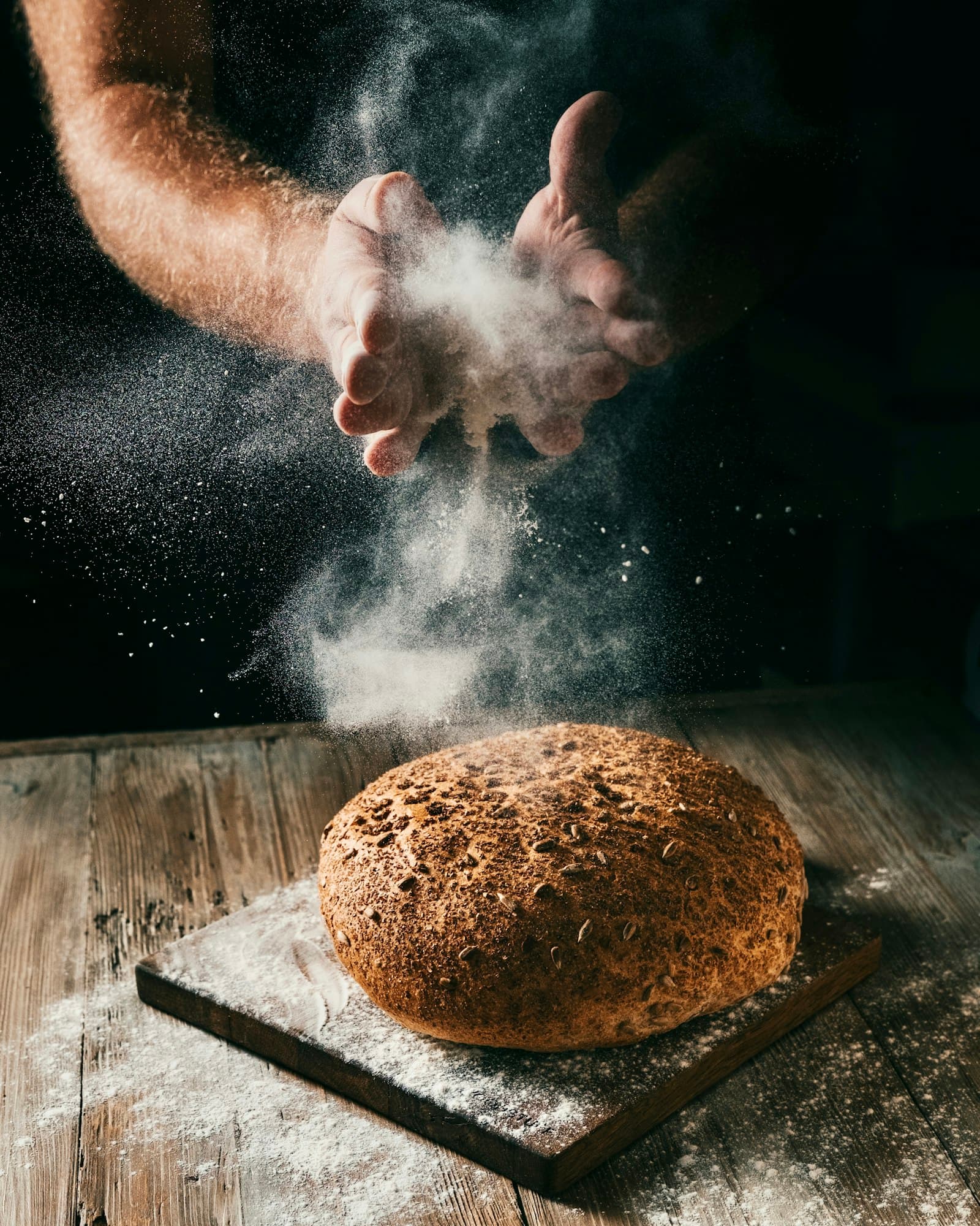 Mãos polvilhando farinha sobre um pão recém-assado